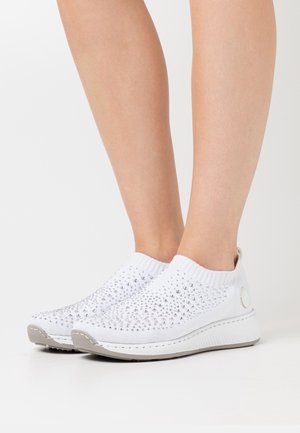 Zapatillas blancas sin cordones con tachuelas plateadas, usadas con los pies descalzos, confeccionadas con tejido de punto y suelas gruesas de goma.