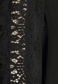 Tissu noir avec des détails en dentelle complexe présentant des motifs floraux et géométriques, offrant un contraste texturé sur un fond uni.
