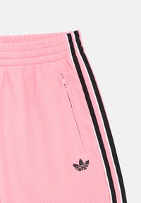 Ροζ τζόγκερ από δίχτυ με μαύρες και λευκές ρίγες στο πλάι, με τσέπη με φερμουάρ και μικρό μαύρο λογότυπο στο πόδι.