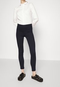 Námořnické modré legíny z elastického materiálu s vysokým pasem, kombinované s bílou košilí s límečkem a černými botami na klouzání. Jednoduché designové prvky.