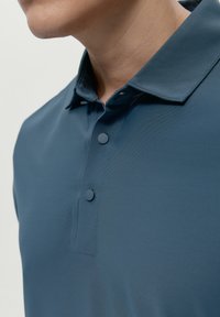 Polo shirt blu scuro con tessuto testurizzato, due bottoni al colletto e design del colletto classico.