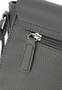 Grijze, gestructureerde leren tas met een ritsafsluiting, voorzien van een zilveren ritstrekkertje en gestikte accenten. Compact ontwerp, gladde afwerking.