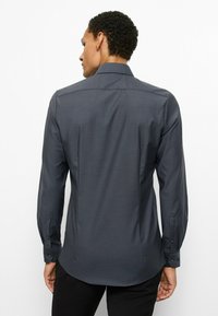 Dunkelgraues Langarmhemd mit dezentem geometrischem Muster, Knopfmanschetten, einem Kentkragen und einer taillierten Passform mit geschwungenen Saumlinien.