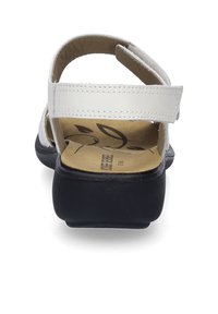 Hvid lædersandal med sort gummisål. Har en justerbar rem og polstret indersål. Bagfra ses det åbne design og sømdetaljer.