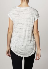 Lehký top s krátkým rukávem v krémové barvě s šedým melírováním, zaobleným lemem a volným střihem, nošený s černými legínami.