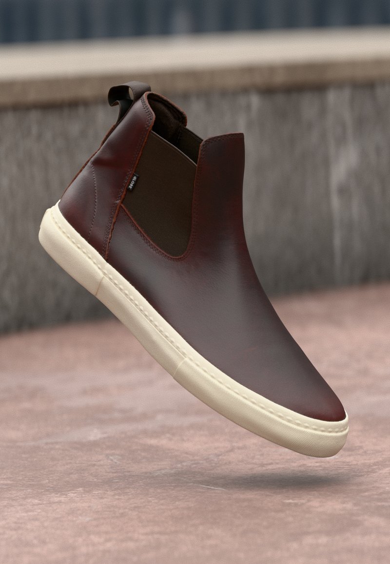 Hnědé kožené kotníkové boty s elastickými bočními panely, hladkým povrchem, bílou gumovou podrážkou a minimalistickým designem.