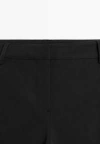 Pantalon noir habillé avec passants de ceinture et fermeture avant cachée, présenté de la taille jusqu'à mi-cuisse sur un fond uni.