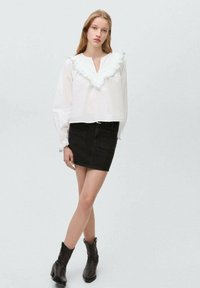 White blouse with a ruffled mint collar and long sleeves, paired with a black denim mini skirt and black ankle boots.
