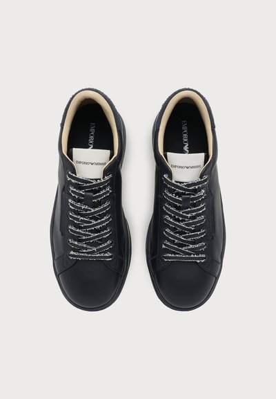 Paire de baskets en cuir noir Emporio Armani avec des lacets blancs et noirs, une doublure intérieure beige et des étiquettes de languette de marque, vues de dessus.