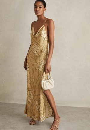 Satin yellow dress with floral outline, cowl neck, adjustable straps, flowing silhouette, paired with a white puff bag and tan sandals.