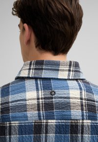 Blauwe geruite flanellen overhemden met een knoop aan de achterkant, in contrasterende donkerblauwe en lichtblauwe, witte en bruine ruitpatronen.