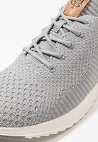 Sneaker grigia in maglia con tomaia testurizzata, lacci tono su tono e suola in gomma leggera. Include un piccolo accento in pelle tan sulla linguetta.