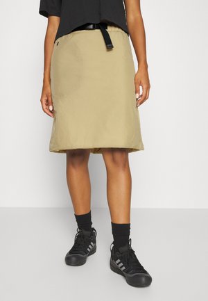 Saia caqui com cintura ajustada e detalhe de cinto, feita de material leve, combinada com sapatilhas e meias pretas.