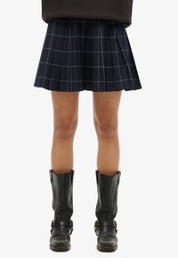 Falda plisada azul marino con patrón de cuadrícula blanca, combinada con botas negras hasta la rodilla con hebillas y textura resistente.