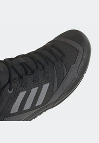 Chaussure de randonnée noire Adidas Terrex avec trois bandes réfléchissantes, embout durable et laçage sécurisé sur une tige texturée.