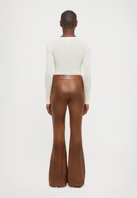 Long-sleeve, fitted cream top with a thin seam at the center back, paired with high-waisted, shiny brown flared trousers.