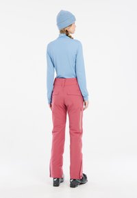 Light blue long-sleeve top, pink ski pants with side zippers, and black ski boots. The outfit features a fitted silhouette and contrasting colors.