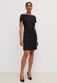 Schwarzes, eng anliegendes Kleid mit Bootsausschnitt und kurzen Ärmeln. Hergestellt aus glattem Stoff, endet es über dem Knie und hat kein sichtbares Muster.