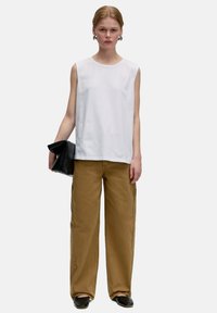 Haut sans manches blanc, pantalon large beige, et pochette noire. Tissu lisse, coupe décontractée, et design simple sans motifs ni embellissements visibles.