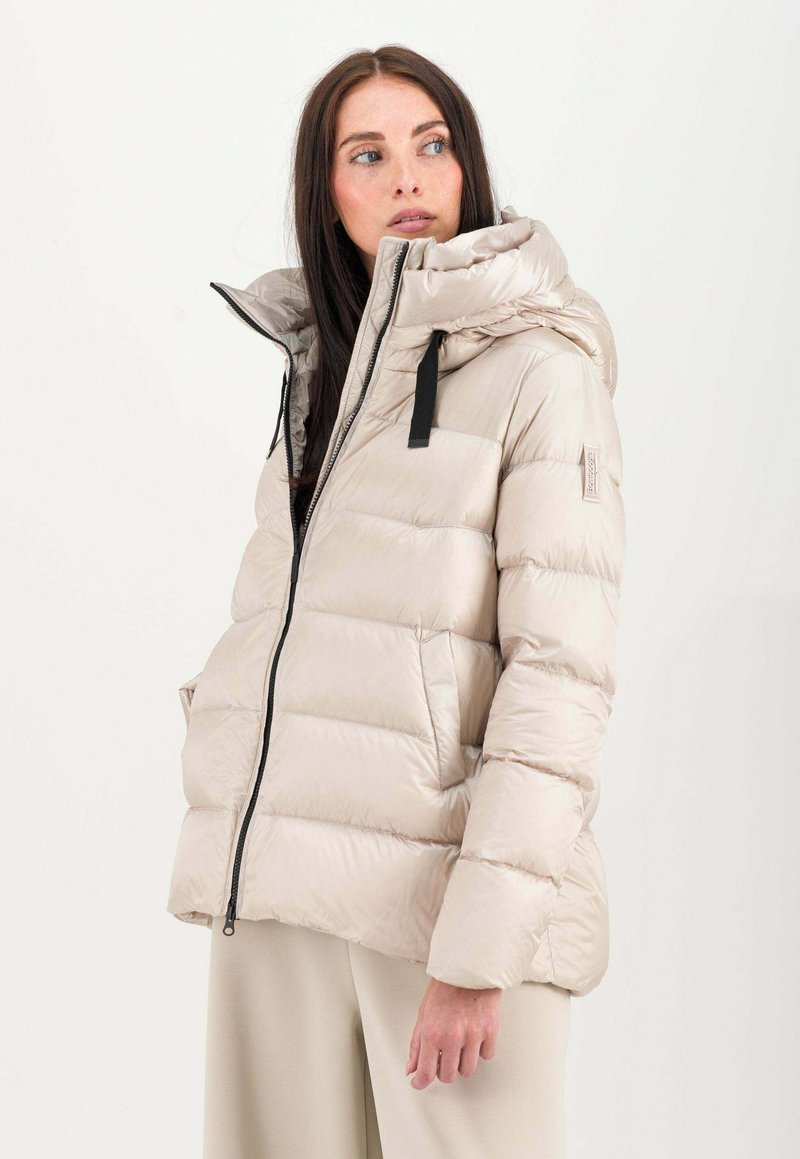 Gepolsterte Pufferjacke in Hellbeige mit hohem Kragen, Frontreißverschluss und schwarzen Hardware-Akzenten. Glatte Textur mit gesteppten Abschnitten.