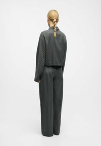 Graue, gestreifte, verkürzte Jacke und weit geschnittene Hose. Glattes Material, lockere Passform und auffällige vertikale Linien. Rückansicht hervorgehoben.