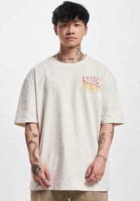Cremefarvet oversized t-shirt lavet af bomuld. Har en farverig grafisk design på venstre bryst. Korte ærmer og en rund halsudskæring.