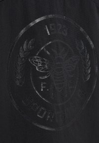 Svart sporttyg med en tonad präglad cirkulär logotyp som har en bi, lagerblad och året 1923, tillsammans med ordet "SPORTWEAR."