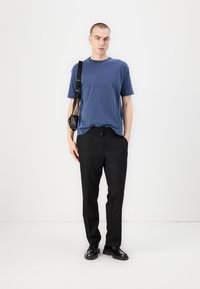 Men's blue cotton t-shirt, relaxed fit, paired with black trousers featuring a drawstring waist. Black shoes and small shoulder bag included.