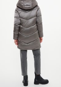 Abrigo acolchado gris con patrón de acolchado en forma de cheurón, capucha y bolsillos delanteros, combinado con pantalones grises y botines negros.