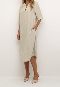 Vestido midi a rayas en beige y blanco, con cuello sin solapa, mangas cortas, bolsillos laterales y un corte ligeramente holgado.