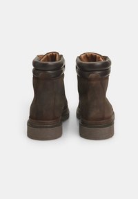 Stivaletti alla caviglia in suede marrone con un colletto in pelle marrone imbottito, suola testurizzata e punta arrotondata. Presentano un design robusto e resistente.
