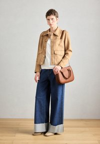 Brun mockajacka med två framfickor, vit topp, breda blå denimjeans med fransar i nederkant, och en brun handväska med axelrem.