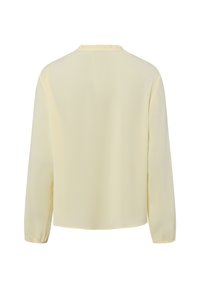 Bluzka z długim rękawem w miękkim, żółtym materiale. Posiada okrągły dekolt z falbaną i luźny krój. Gładka tekstura, bez widocznych wzorów.