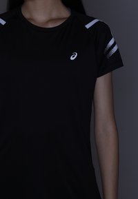 Schwarzes Sport-T-Shirt mit kurzen Ärmeln, weißen Akzenten und einem Logo auf der Brust. Glatte Textur und athletisches Design.