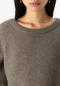 Maglione marrone a maglia con un ampio scollo rotondo, texture morbida e maniche raglan, che mostra un sottile motivo a puntini su tutta la stoffa.