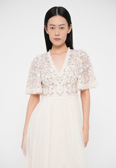 Rochie brodată cu mâneci scurte bufante, decolteu în V și modele florale. Confecționată dintr-un material transparent, ușor; culoare crem deschisă, cu detalii texturate.
