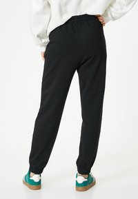 Zwarte sweatpants met een elastische tailleband, taps toelopende boorden en een soepele textuur. Gecombineerd met meerkleurige sneakers met een witte accenten.