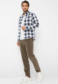 Camicia di flanella a quadri nei colori blu navy, bianco e grigio; abbinata a pantaloni di costina marroni e sneaker bianche; stile con bottoni.