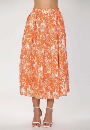 Jupe mi-longue avec imprimé floral tropical orange et blanc, portée avec des sandales blanches à bride cheville et orteils ouverts, sur fond clair.