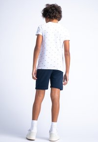 Biały t-shirt z krótkim rękawem z małym niebieskim nadrukiem, w połączeniu z granatowymi szortami. Całość dopełniają białe trampki i skarpetki.