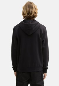 Felpa nera con cappuccio, realizzata in un tessuto testurizzato, maniche lunghe e orlo a coste. Presenta un design cucito a doppio filo e una vestibilità comoda.