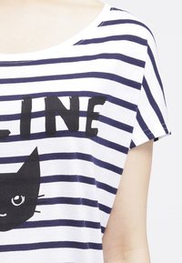 Camiseta blanca con rayas horizontales en navy. Presenta un gráfico de un gato negro con ojos grandes y la palabra "LINE" en negrita y en color negro encima.