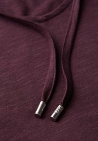 Sweat à capuche bordeaux en tissu texturé, avec deux cordons de serrage dotés d'embouts métalliques, mettant en avant un design décontracté.