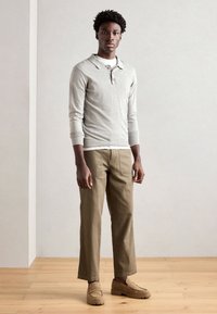 Grå longsleeve polo shirt med krave, kombineret med khaki bukser og beige slip-on sko, alt sat mod en neutral baggrund.