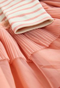 Top a righe beige e rosa in cotone con gonna in tulle gonfiata di un morbido rosa, caratterizzata da una texture plissettata e design a strati.
