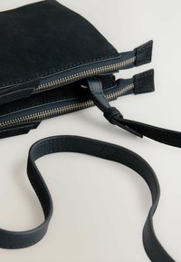 Sort ruskinds crossover taske med en struktureret overflade, der har lynlåslukning, læderrem og dobbelt rum.