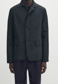 Giacca leggera nera con design a colletto, chiusura con un solo bottone e due tasche frontali. Texture liscia e stile minimalista.