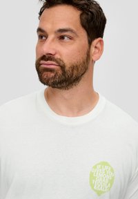 Witte katoenen t-shirt met een ronde halslijn. Heeft een lichtgroene geprinte citroentekening en tekst: "ALS HET LEVEN JE CITROENEN GEEFT, PAK TEQUILA EN ZOUT."