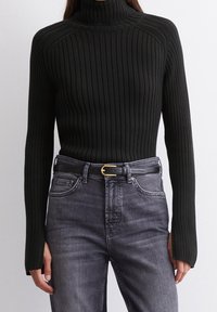 Pull en maille côtelée noir avec col roulé et manches longues, associé à un jean en denim gris et une ceinture noire avec une boucle dorée.