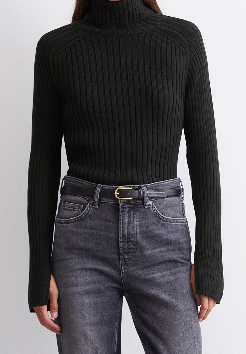 Pull en maille côtelée noir avec col roulé et manches longues, associé à un jean en denim gris et une ceinture noire avec une boucle dorée.